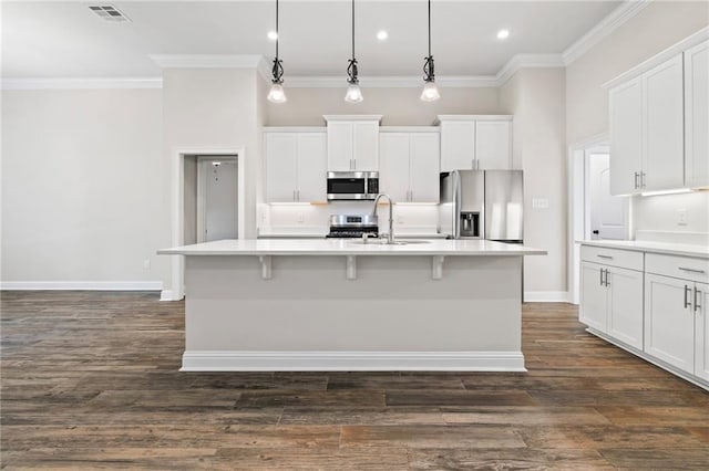 kitchen featuring white cabinets, appliances with stainless steel finishes, decorative light fixtures, and a kitchen island with sink