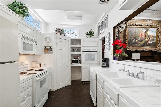 kitchen featuring white appliances, sink, tile countertops, backsplash, and white cabinetry