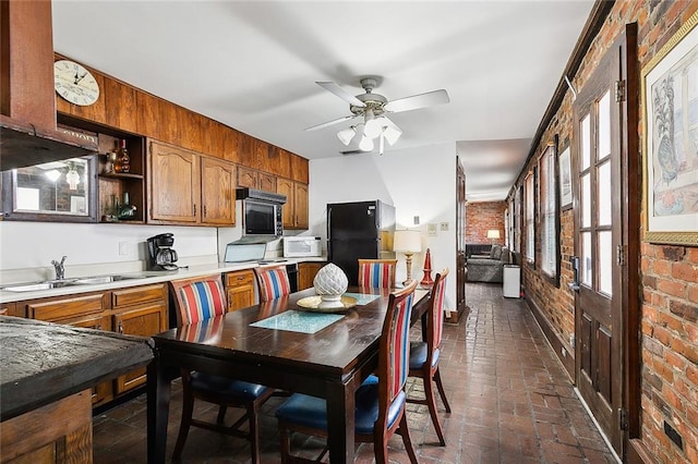 dining space with ceiling fan, brick wall, and sink