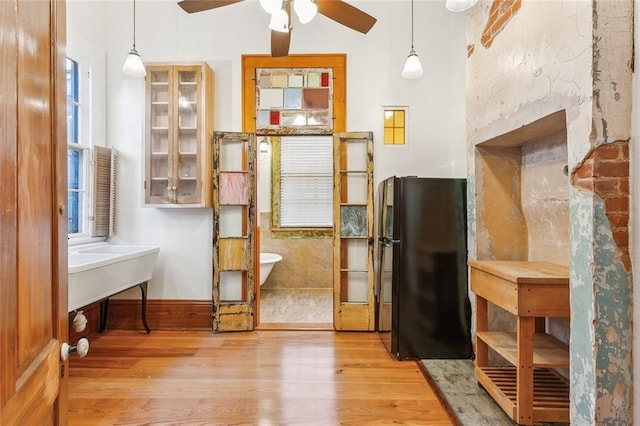 interior space with light hardwood / wood-style floors, hanging light fixtures, black refrigerator, and ceiling fan