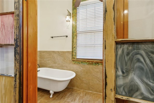 bathroom featuring a tub to relax in, tile walls, and a healthy amount of sunlight