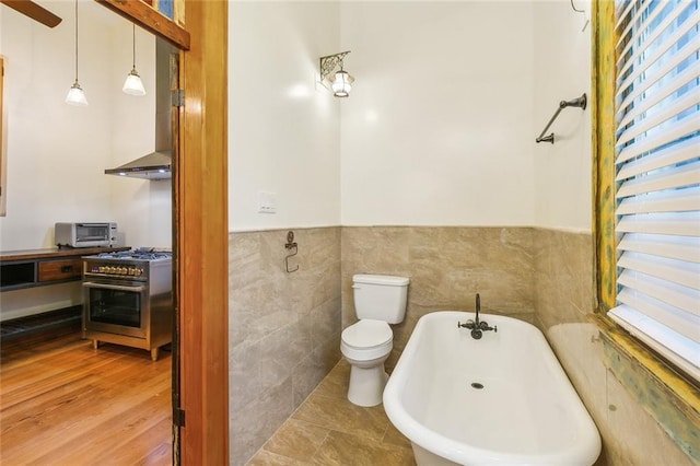 bathroom with tile walls, hardwood / wood-style flooring, toilet, and a washtub