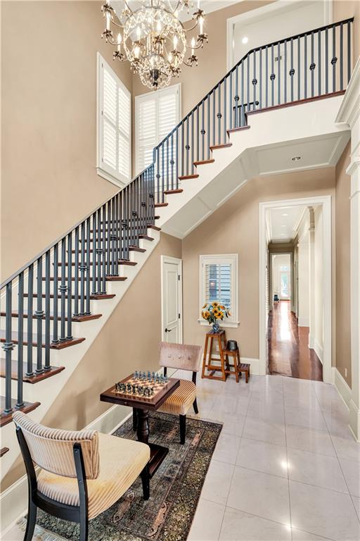 stairway featuring a high ceiling, ornamental molding, an inviting chandelier, tile patterned floors, and ornate columns