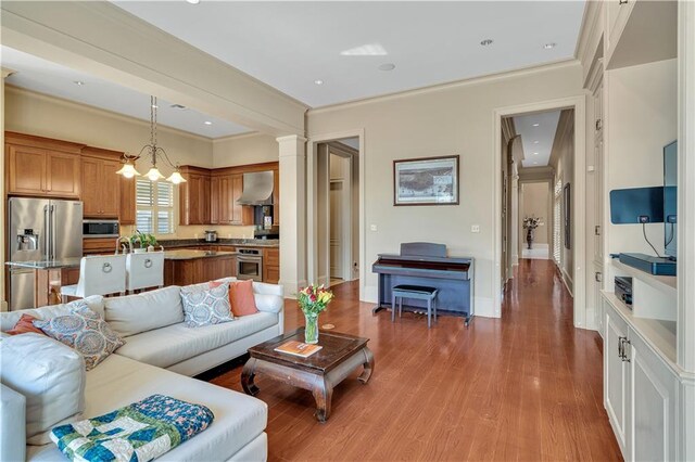 living room featuring light hardwood / wood-style floors, a notable chandelier, crown molding, and decorative columns