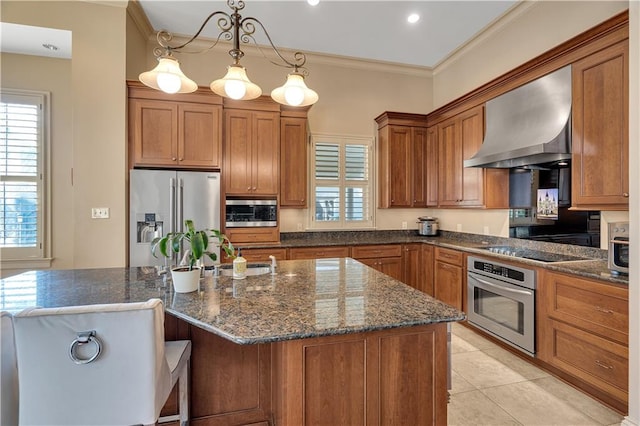 kitchen with ornamental molding, a kitchen island, appliances with stainless steel finishes, decorative light fixtures, and wall chimney exhaust hood