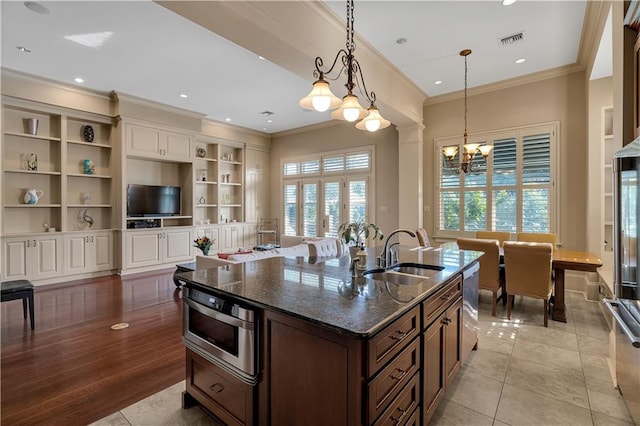 kitchen with light hardwood / wood-style floors, sink, ornamental molding, dark stone countertops, and an inviting chandelier