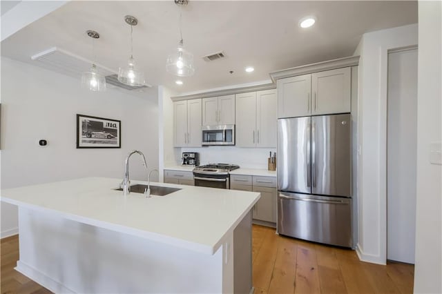 kitchen featuring visible vents, light wood-style flooring, an island with sink, a sink, and appliances with stainless steel finishes