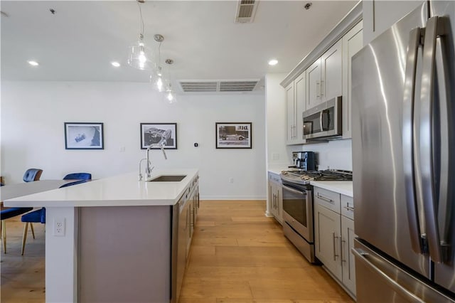 kitchen featuring a breakfast bar area, visible vents, gray cabinetry, a sink, and appliances with stainless steel finishes