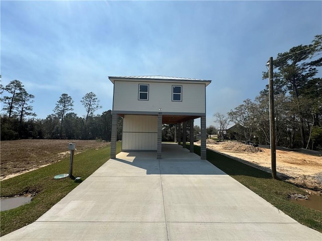 beach home with a carport, concrete driveway, a front yard, and metal roof