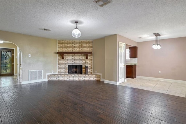 unfurnished living room with light hardwood / wood-style flooring, a textured ceiling, and a brick fireplace