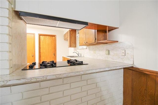 kitchen with range hood, backsplash, sink, and black gas cooktop