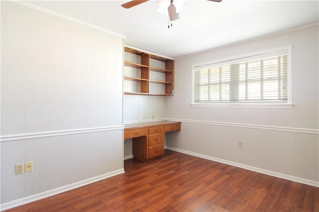 unfurnished office with built in desk, crown molding, dark hardwood / wood-style floors, and ceiling fan