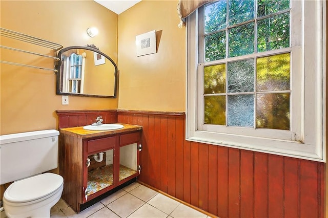 bathroom with wooden walls, sink, toilet, and tile patterned flooring