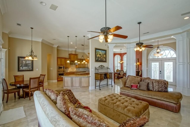 tiled living room featuring french doors, ornate columns, ornamental molding, and ceiling fan with notable chandelier