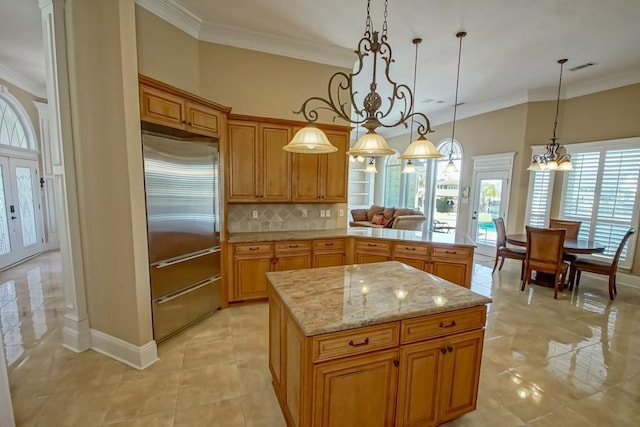 kitchen featuring tasteful backsplash, a kitchen island, crown molding, decorative light fixtures, and built in refrigerator