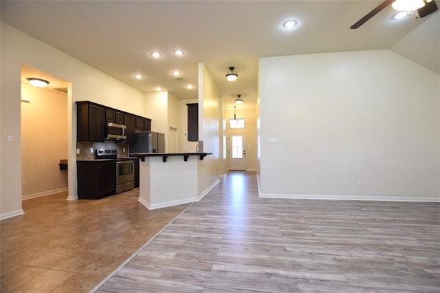 kitchen featuring light hardwood / wood-style flooring, stainless steel appliances, a breakfast bar, vaulted ceiling, and ceiling fan