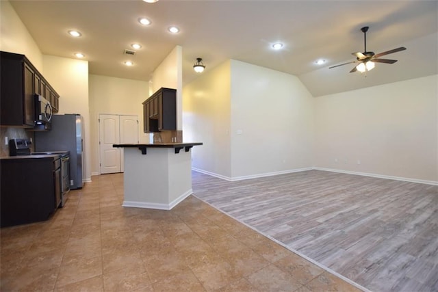 kitchen with light wood-type flooring, a kitchen breakfast bar, ceiling fan, stainless steel appliances, and vaulted ceiling