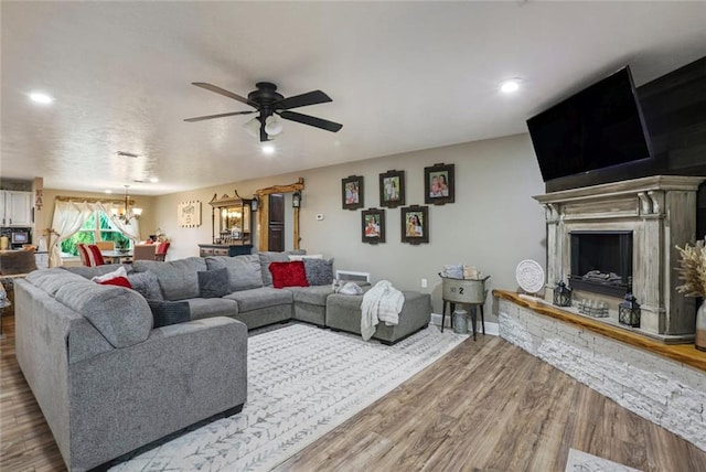 living room with a stone fireplace, hardwood / wood-style floors, and ceiling fan with notable chandelier