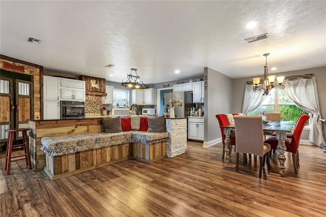 kitchen featuring appliances with stainless steel finishes, hanging light fixtures, white cabinetry, hardwood / wood-style floors, and an inviting chandelier