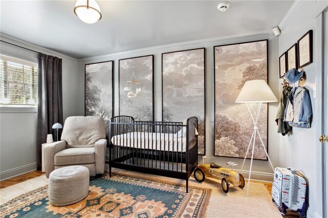 bedroom featuring a nursery area, baseboards, ornamental molding, and wood finished floors