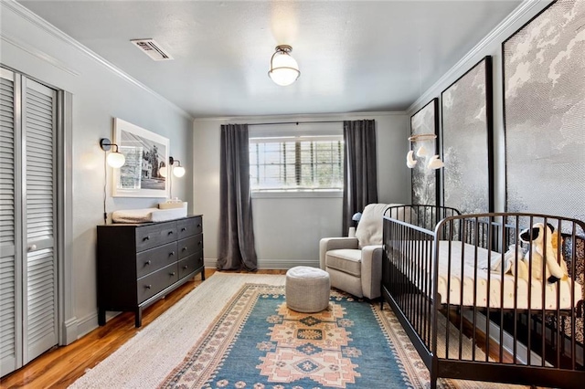 bedroom with wood finished floors, visible vents, a crib, and baseboards