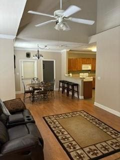 living area featuring ceiling fan with notable chandelier, baseboards, crown molding, and wood finished floors