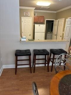 kitchen featuring wood finished floors, baseboards, ornamental molding, freestanding refrigerator, and a kitchen bar