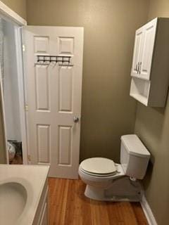 half bath featuring baseboards, vanity, toilet, and wood finished floors