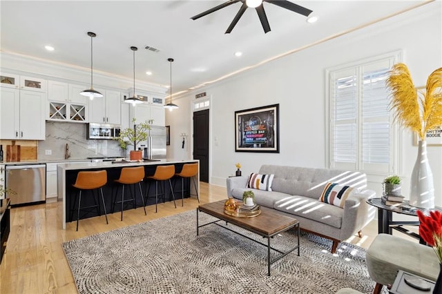 living room with light hardwood / wood-style floors, ornamental molding, sink, and ceiling fan