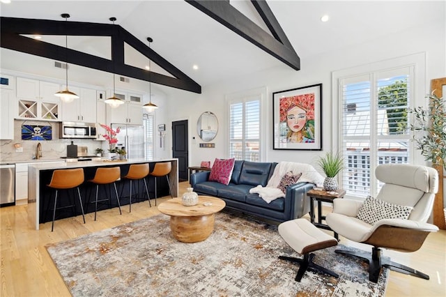 living room with sink, lofted ceiling with beams, and light hardwood / wood-style flooring