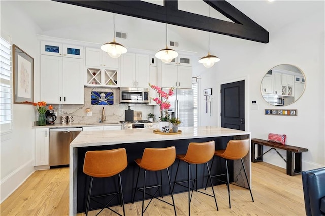 kitchen featuring a kitchen island with sink, lofted ceiling with beams, stainless steel appliances, and white cabinetry