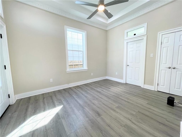 unfurnished bedroom with light wood-type flooring, ceiling fan, and a raised ceiling