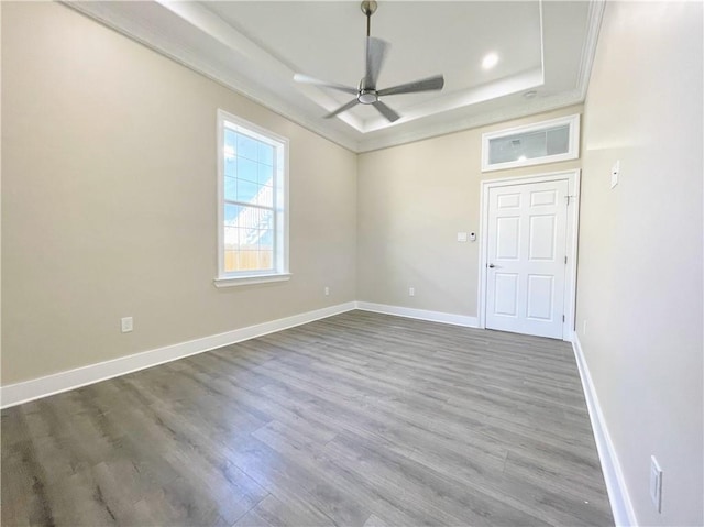 empty room with hardwood / wood-style flooring, ceiling fan, crown molding, and a tray ceiling