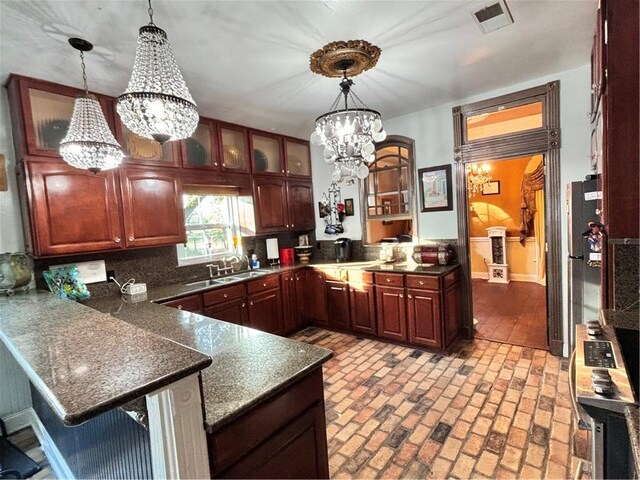 kitchen featuring tasteful backsplash, a notable chandelier, kitchen peninsula, sink, and hanging light fixtures