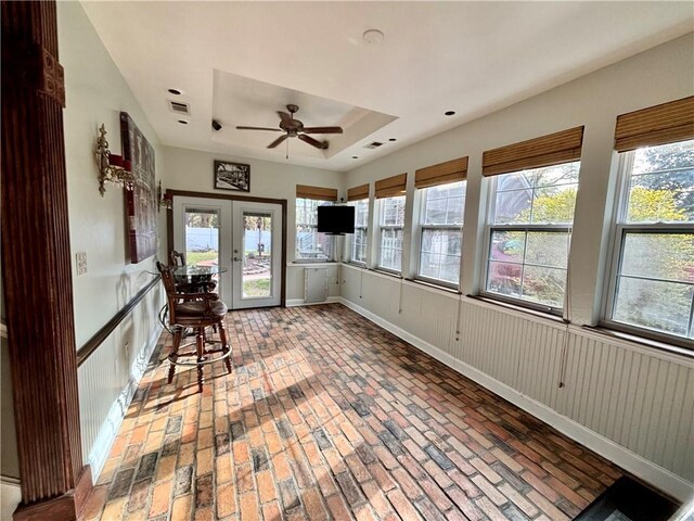 unfurnished sunroom with french doors, ceiling fan, plenty of natural light, and a raised ceiling