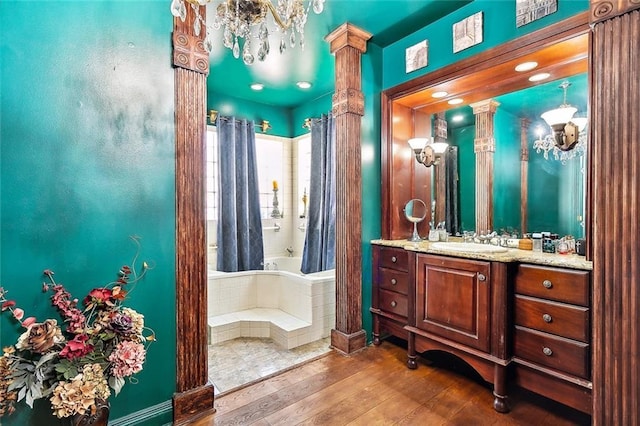 bathroom featuring decorative columns, tiled tub, vanity, and hardwood / wood-style floors