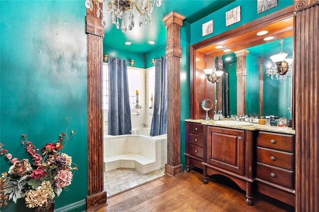 bathroom featuring decorative columns, tiled tub, vanity, and hardwood / wood-style floors