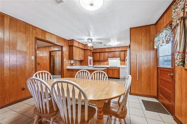 dining room featuring ceiling fan, wood walls, and light tile patterned floors