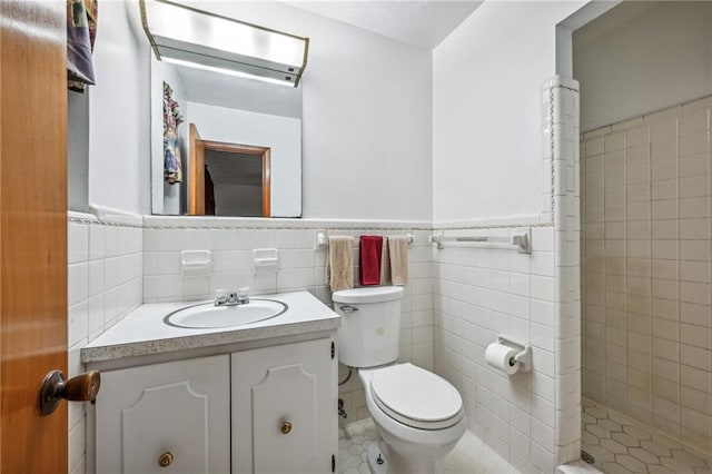 bathroom featuring toilet, vanity, tile walls, and tiled shower