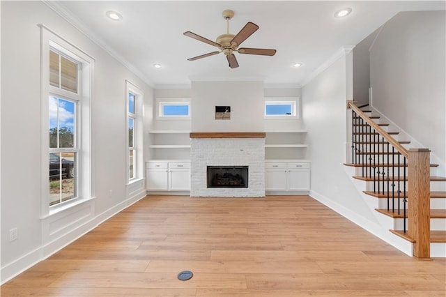 unfurnished living room with ornamental molding, a stone fireplace, light wood-type flooring, and ceiling fan