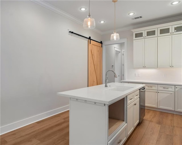 kitchen featuring sink, a barn door, light hardwood / wood-style floors, white cabinets, and a center island with sink