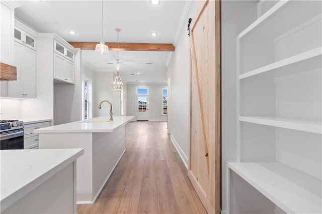 kitchen featuring light wood-type flooring, a barn door, gas stove, pendant lighting, and white cabinets