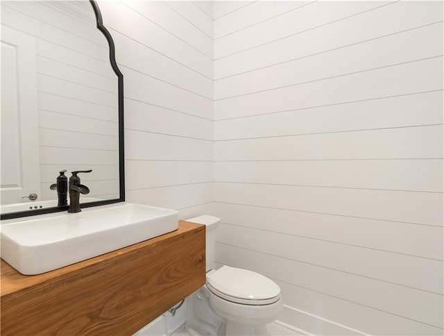 bathroom with vanity, wooden walls, and toilet