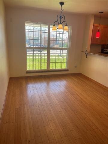 unfurnished dining area with an inviting chandelier, plenty of natural light, and wood finished floors