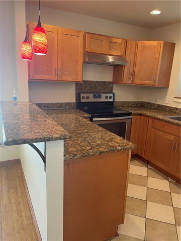 kitchen with dark stone counters, stainless steel electric range oven, decorative light fixtures, a peninsula, and under cabinet range hood