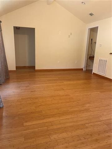 empty room featuring vaulted ceiling, light wood finished floors, and visible vents