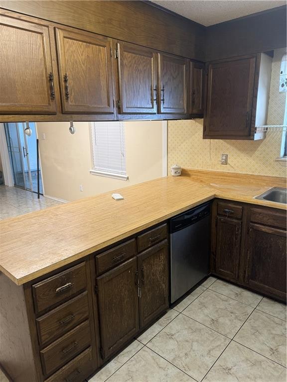 kitchen featuring sink, dark brown cabinets, kitchen peninsula, stainless steel dishwasher, and decorative backsplash