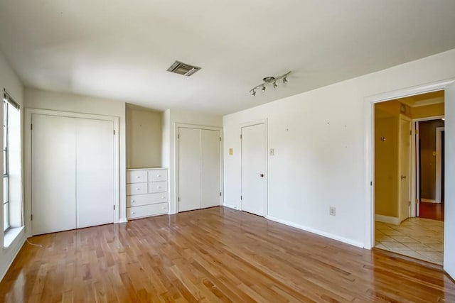 unfurnished bedroom with two closets and light wood-type flooring