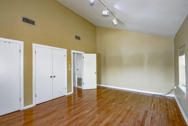 unfurnished bedroom with two closets, high vaulted ceiling, light wood-type flooring, and rail lighting