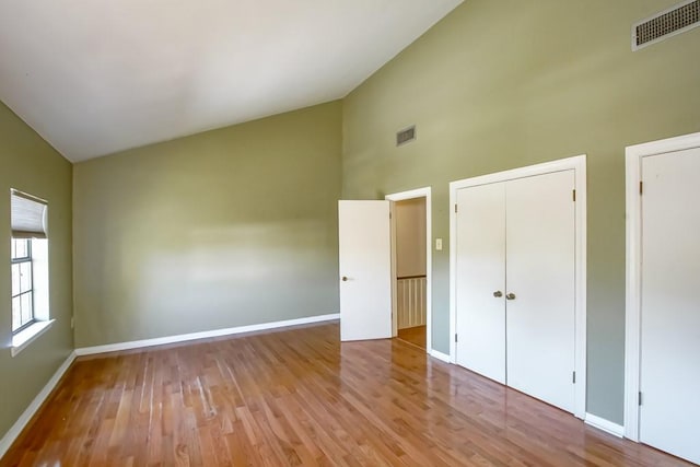 unfurnished bedroom with high vaulted ceiling and light wood-type flooring